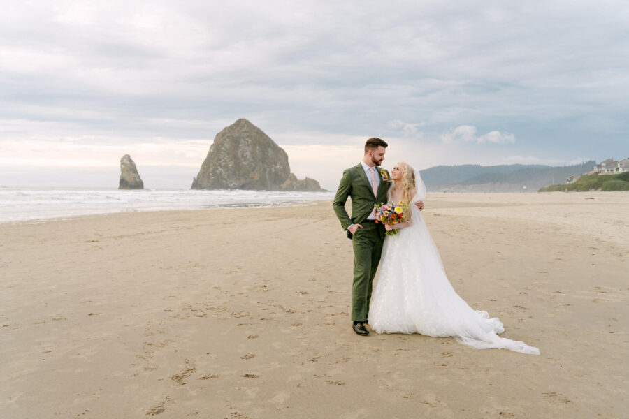 Romantic wedding couple embracing on the sandy shores of Cannon Beach with Haystack Rock in the background.