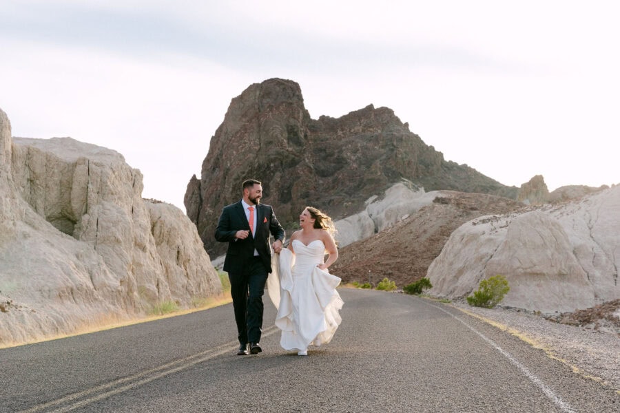 Bride and groom walking hand in hand along a scenic desert road surrounded by the dramatic landscapes of Big Bend National Park.