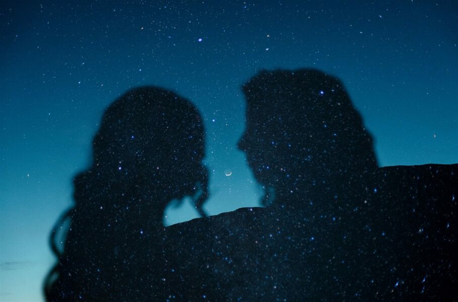 ilhouettes of a couple against a starry night sky with a crescent moon nestled between their profiles.