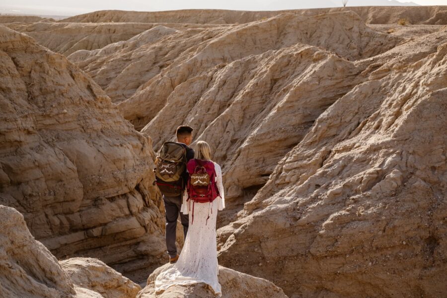 A newlywed couple with 'Just Married' backpacks trekking through a rugged slot canyon, symbolizing the beginning of their journey together.