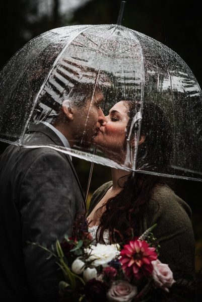 bride and groom kissing under umbrella on a rainy fall day in alaska