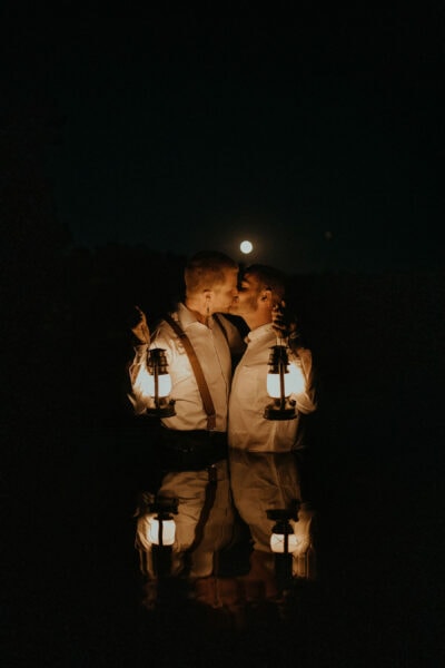 Two men kissing while holding lanterns in a lake