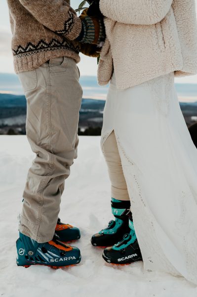 couple standing on top of mountain in ski boots for their Vermont winter elopement