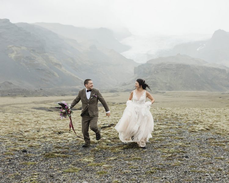A couple running and laughing while looking at each other at their ceremony location in Iceland