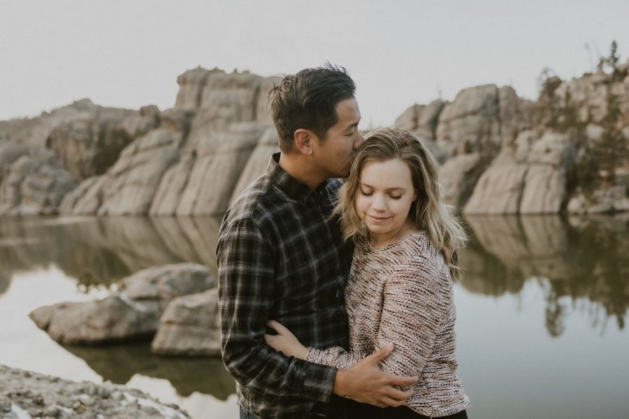 Husband kisses wife on forehead with Sylvan Lake, SD in the background