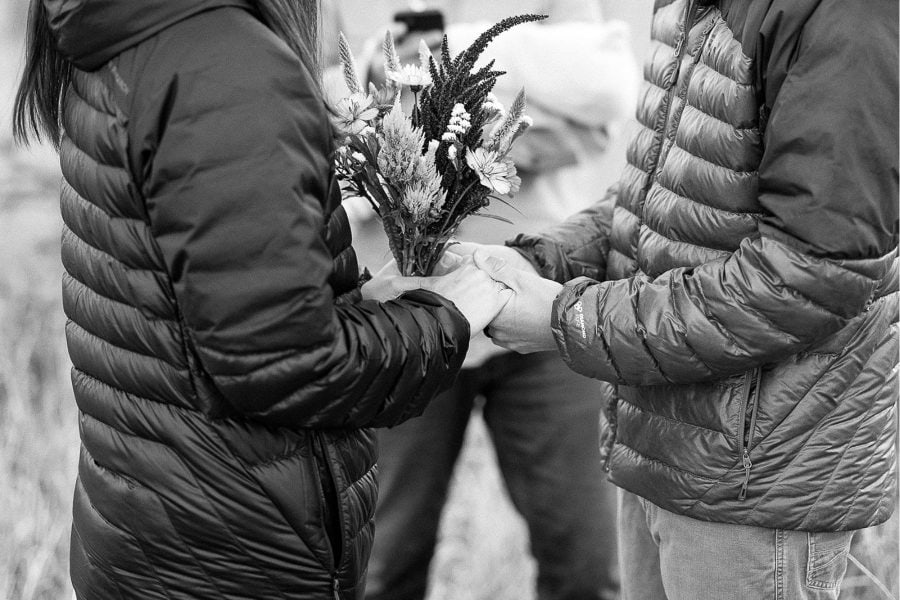 Couple wearing down jackets hold hands during elopement ceremony in Black Hills National Forest