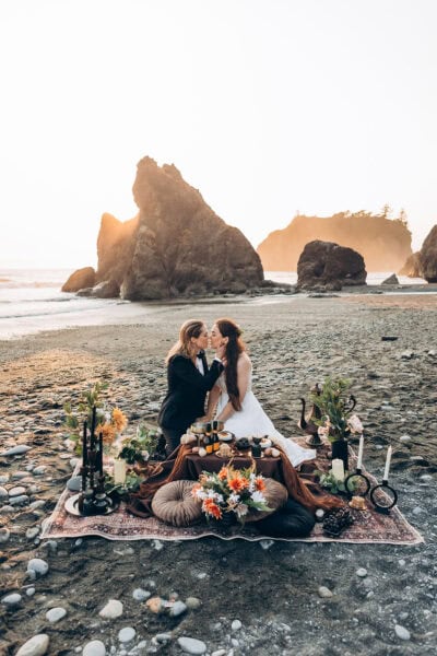 LGBTQ couple kissing during a sunset elopement picnic on Ruby Beach in Olympic National Park, Washington, with sea stacks behind them