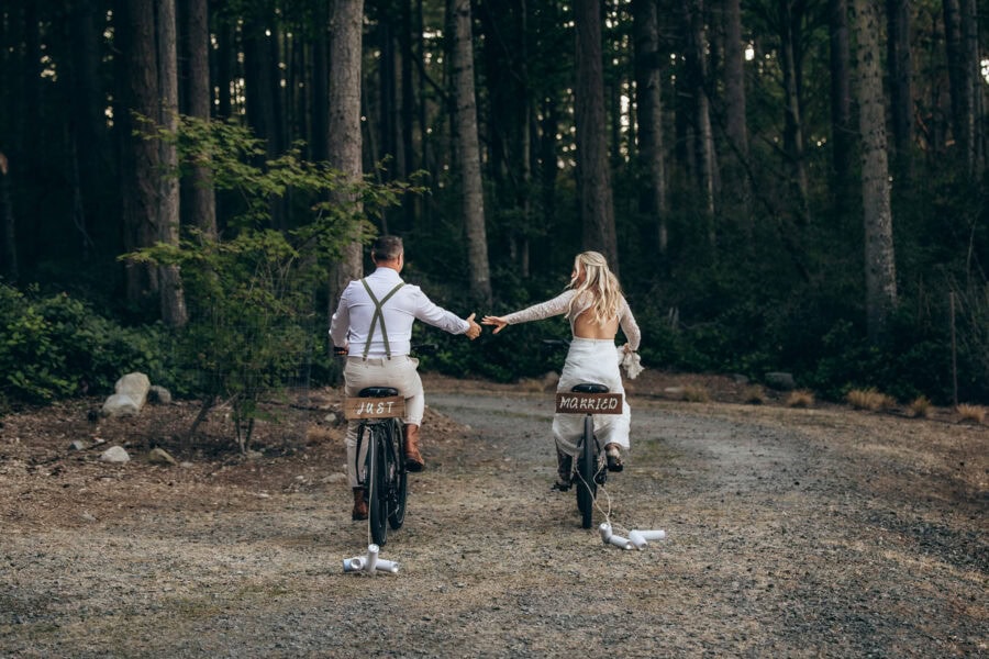 Newly married couple riding bicycles and holding hands on a forest road on Lopez Island in the San Juan Islands, Washington
