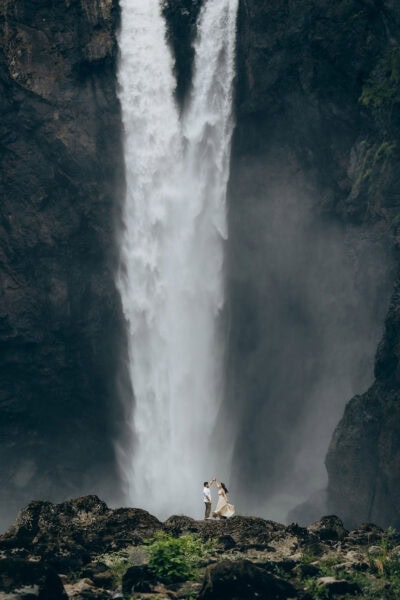 Couple standing on rocks in front of Snoqualmie Falls in Washington, dancing together with the waterfall towering behind them
