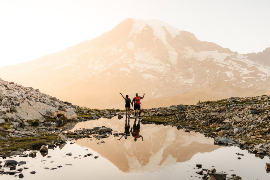 Couple standing at an alpine tarn in Mount Rainier National Park with Mount Rainier reflected in the water during a hiking elopement