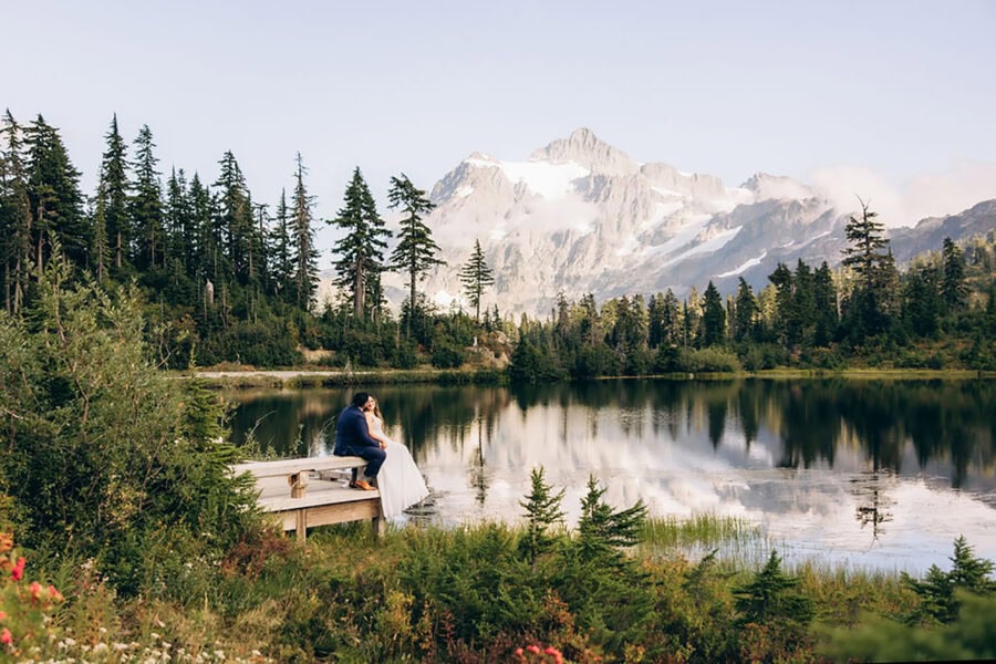 Bride and groom sitting on a wooden dock at Picture Lake in the North Cascades with mountains reflected in the water