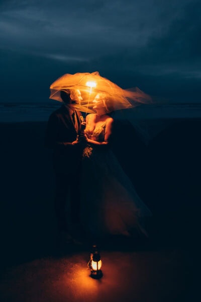 Bride and groom standing under a veil holding a lantern at Hug Point on the Oregon Coast at night