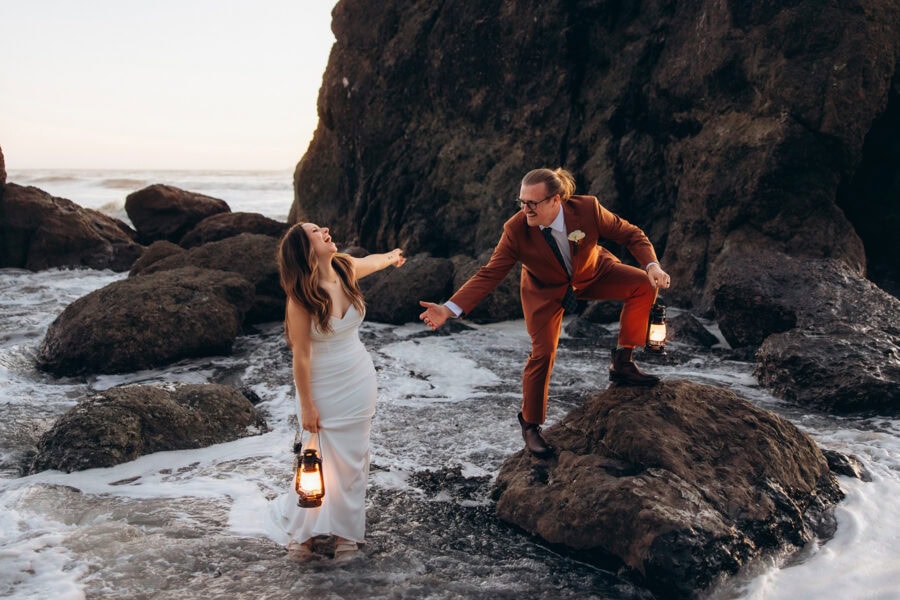 Bride and groom standing on rocks at Rialto Beach in Washington holding lanterns as waves wash around them