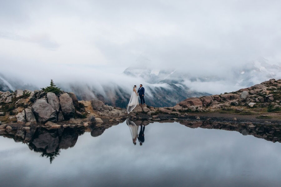 Couple standing at Artist Point near Mount Baker in Washington with mountain fog and reflection in an alpine tarn