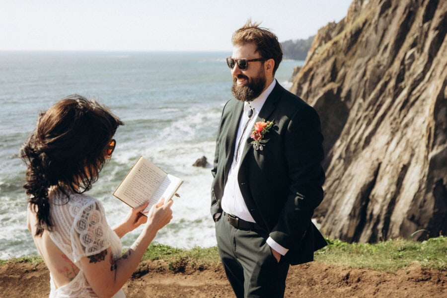 Bride reading handwritten vows to groom at Elk Flats on the Oregon Coast with ocean cliffs in the background