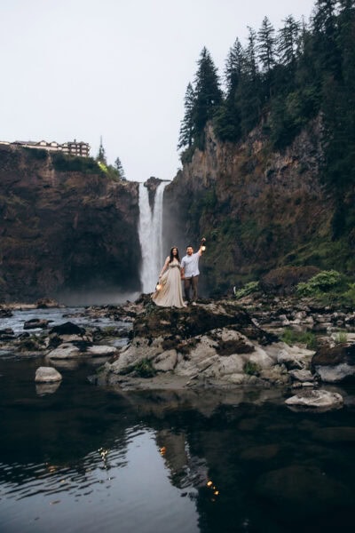 Couple standing on rocks holding lanterns in front of Snoqualmie Falls in Washington during their elopement