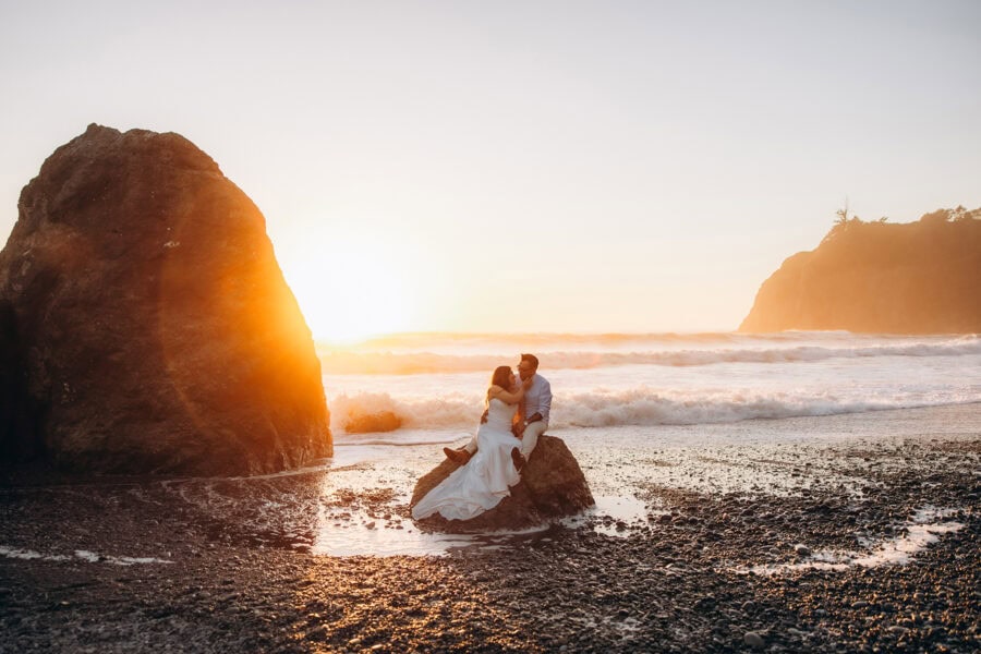 Couple sitting on a rock at sunset during a Washington coast elopement with waves crashing behind them
