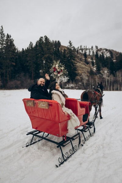 Newlywed couple riding in a red horse-drawn sleigh during a snowy winter elopement in Leavenworth, Washington