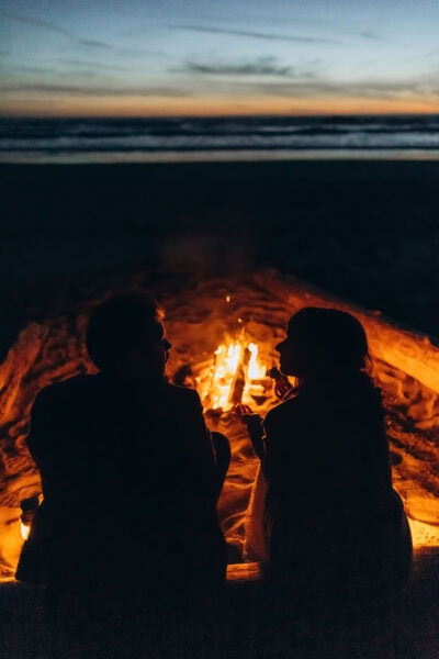Couple sitting by a bonfire on the Oregon Coast at dusk after their elopement