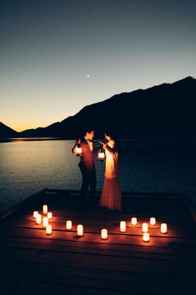 Couple holding lanterns on a dock at Lake Crescent in Olympic National Park at dusk with candles arranged around them