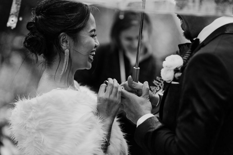 Couple exchanging rings during wedding ceremony under an umbrella