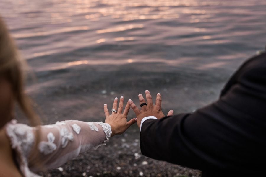 Bride and groom showing their rings for a photo over the sunset reflection in the water