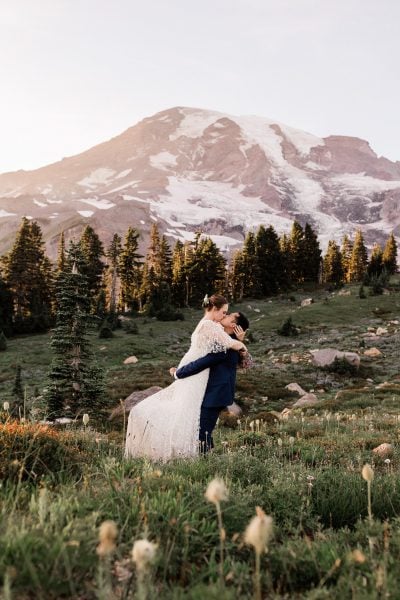 Groom lifting up bride for a kiss in wildflowers at Mount Rainier
