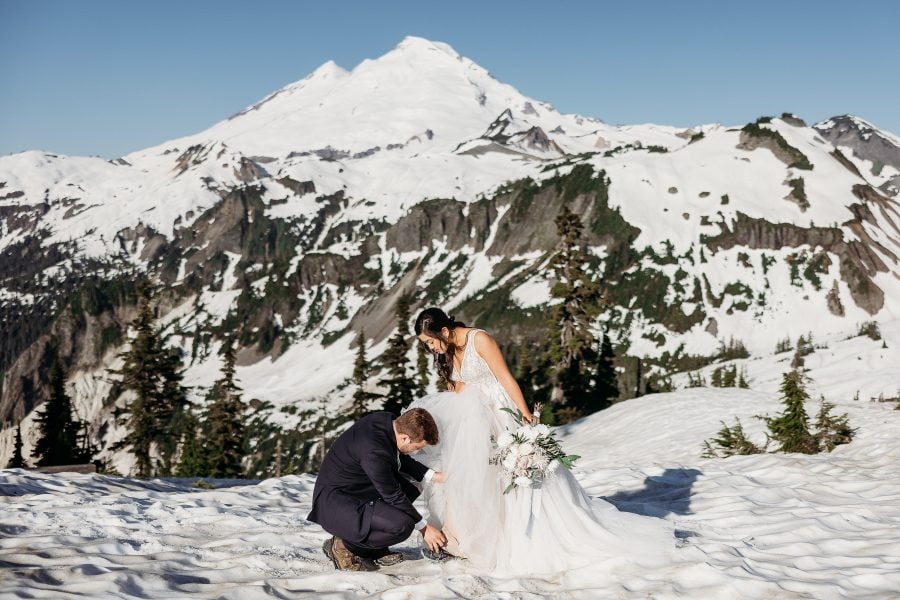 Groom tying Bride's shoe with Mount Baker in the background