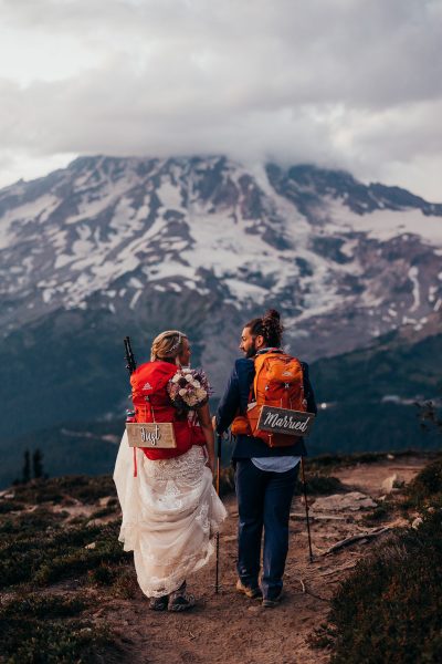 bride and groom hiking on a trail with mount rainier in the background