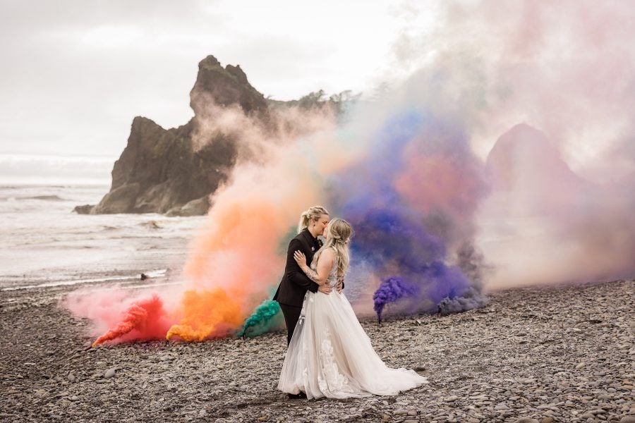 LGBTQ+ wedding ceremony with rainbow smoke bombs behind couple