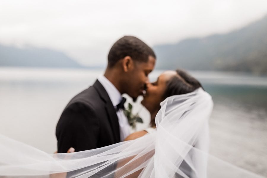Newlyweds kissing at Lake Crescent with veil in focus
