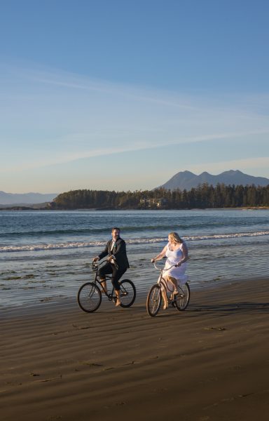 couple riding bikes for their elopement ion a beach n Tofino