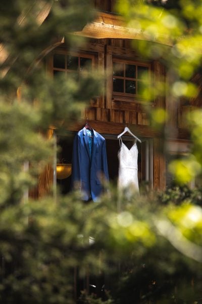 Wedding dress and suit in front of a log cabin
