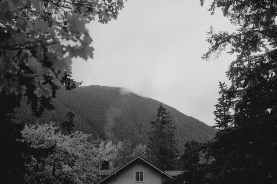 A black and white image of Lake Crescent Lodge with smoke trailing from the fireplace on a cold fall day.