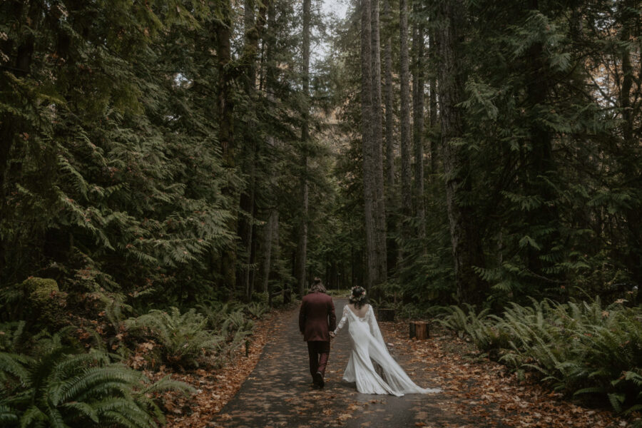 A couple walks away from the camera on a pathway covered in leaves.