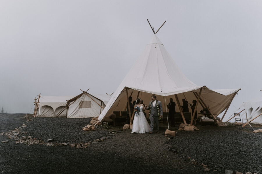 A couple exits the Crystal Sky Camp tent after their wedding ceremony, surrounded by fog-covered mountains.