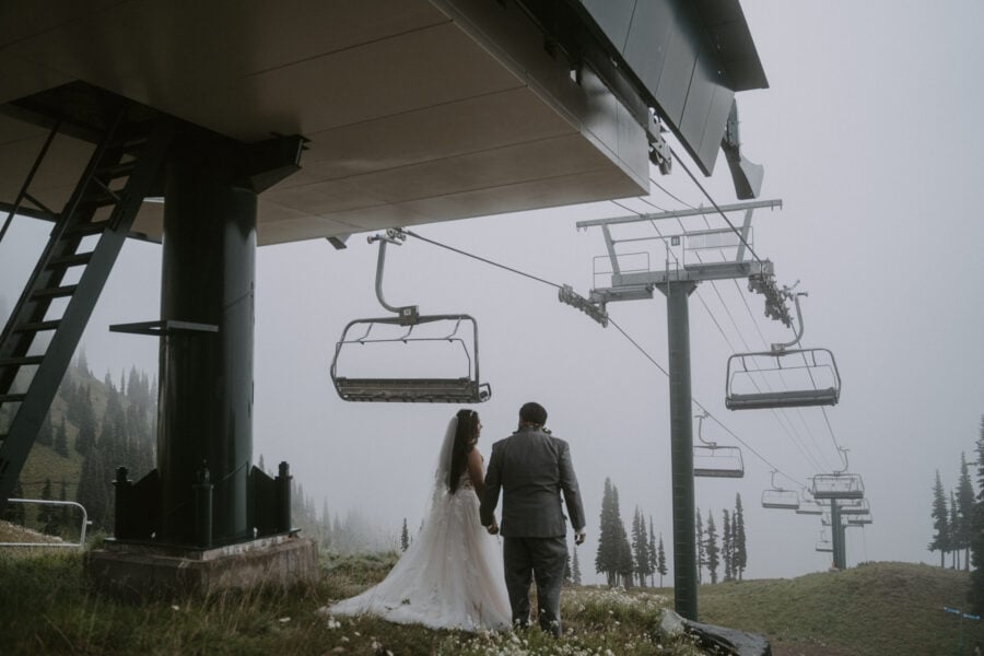 Jesus and Jocelyn in wedding attire, holding hands, overlooking Crystal Mountain with a ski lift emerging through the fog