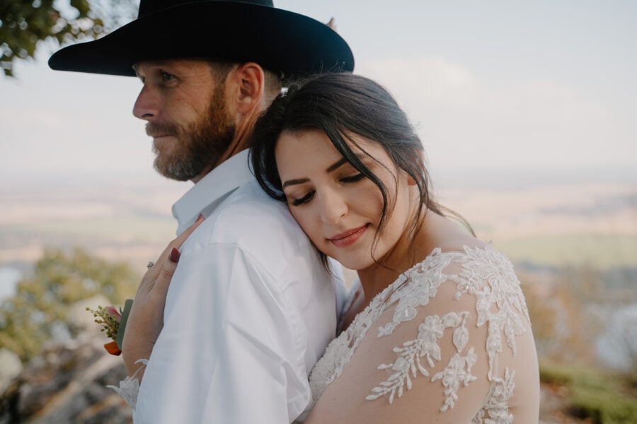 photo of bride hugging groom from the back on top of a mountain