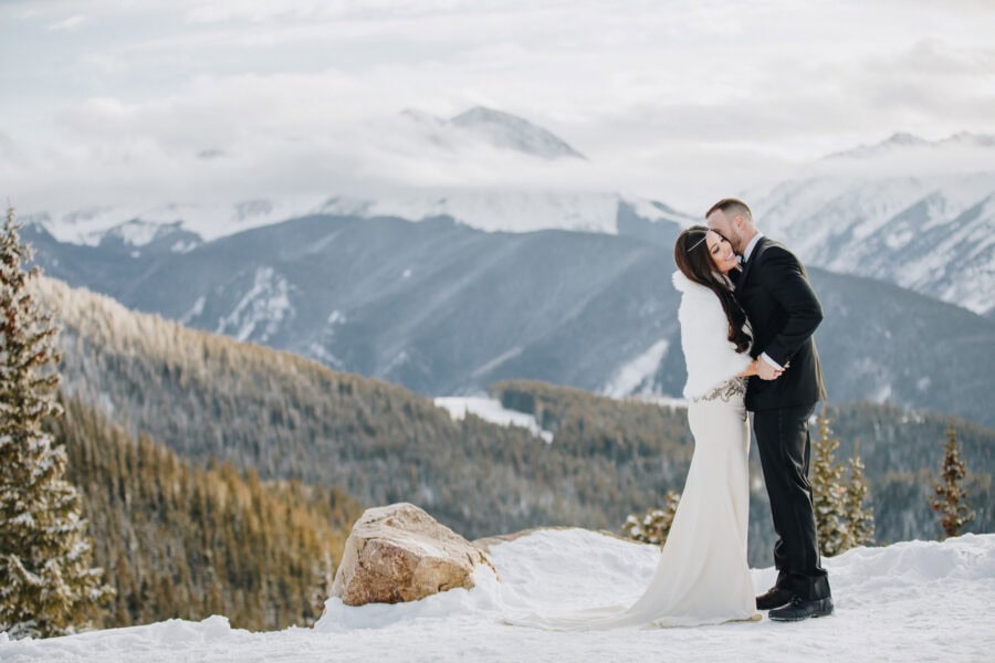bride and groom kissing on top of a snowy mountain