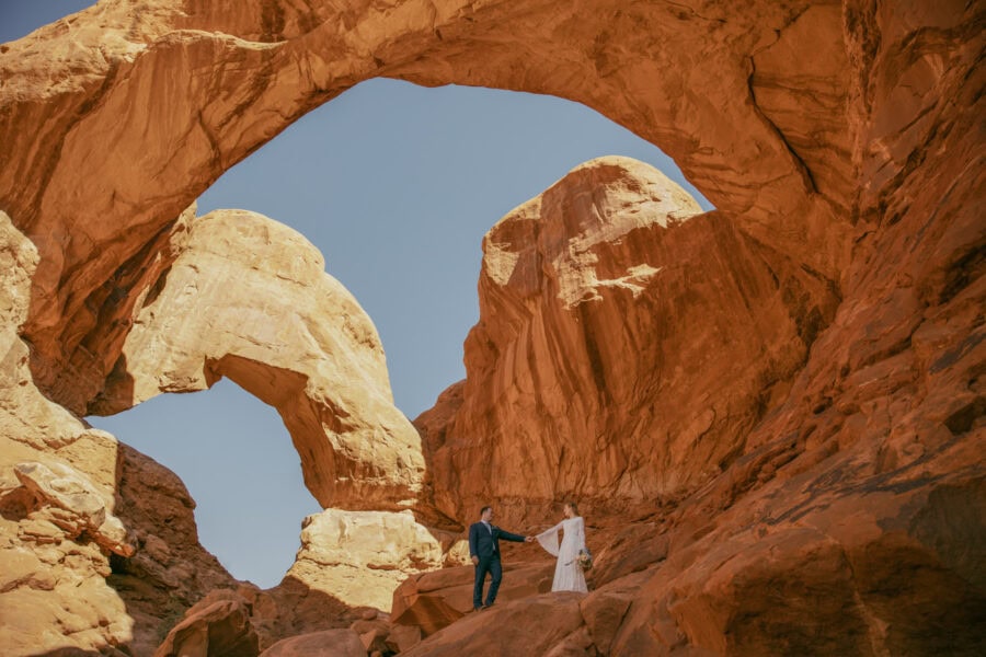 A married couple in standing under Double Arch in Arches National Park