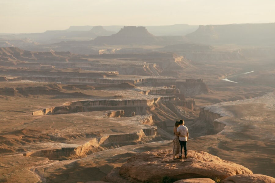 An engaged couple is looking out from the edge of the rim in Canyonlands National Park