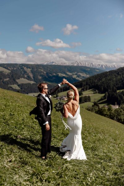 Elopement Couple dancing on a green hill with mountains and a blue sky in the Dolomites in Italy