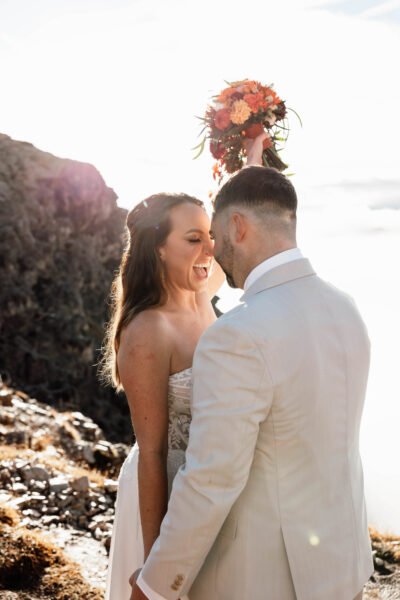 Bride and Groom at Elopement when sun is rising behind them, Bride is holding a bouquet and screaming out of joy
