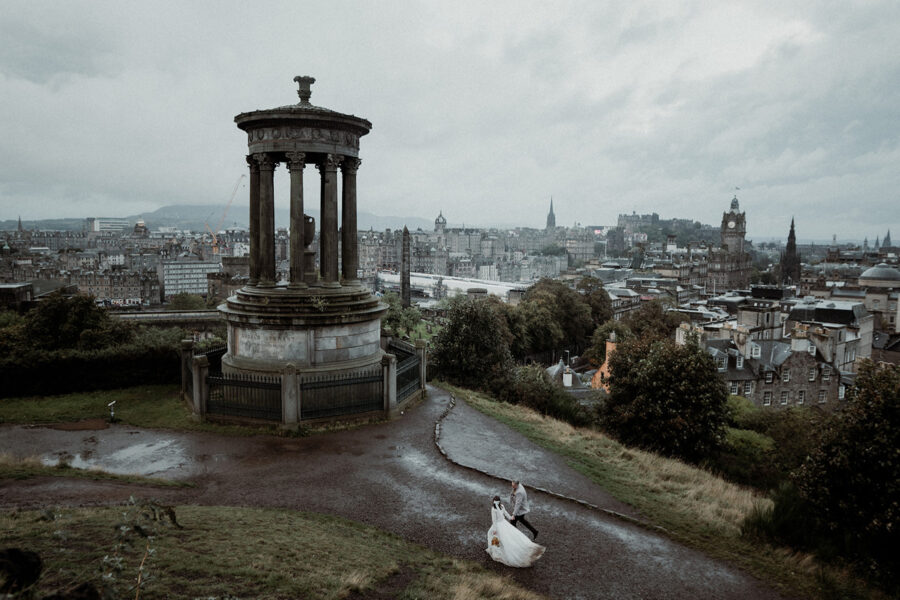 Bride and groom walking together on Calton Hill in Edinburgh with a view of the city