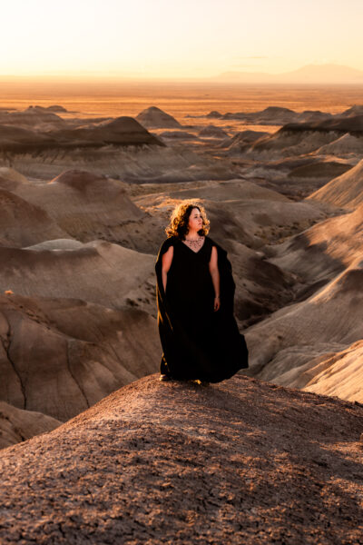A couple in the Painted Desert, one wearing a dramatic black wedding dress with a cape, sharing a tender moment.