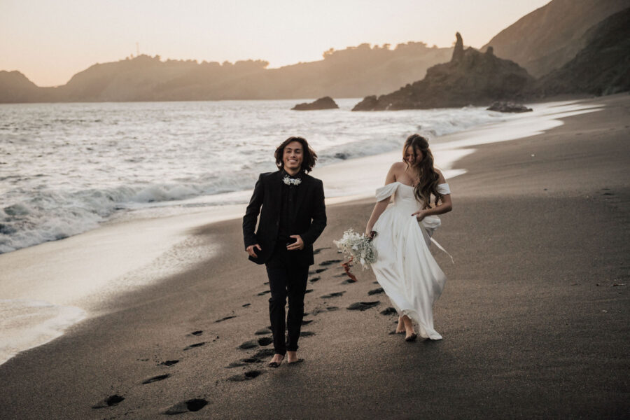 Elopement couple celebrating with a kiss on a secluded black sand beach, surrounded by dramatic coastal cliffs in San Francisco