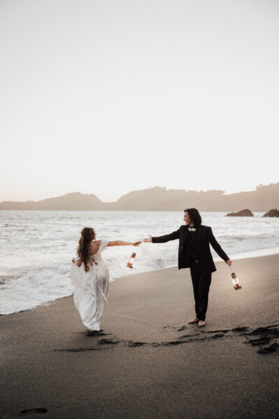 Couple standing on the black sand beach at sunset during their San Francisco elopement, with waves crashing behind them
