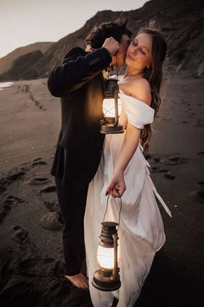 Candid moment of a couple sharing a kiss on Baker Beach with the Golden Gate Bridge in the background