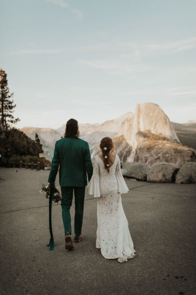 Elopement couple posing on the edge of a rocky overlook with Half Dome glowing at sunset