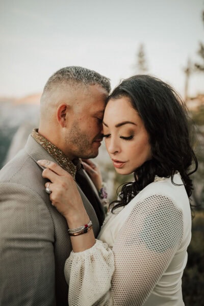 Elopement couple posing on the edge of a rocky overlook with Half Dome glowing at sunset